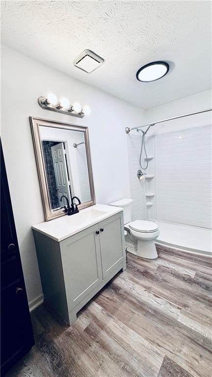 bathroom featuring vanity, a textured ceiling, toilet, a shower, and wood finished floors