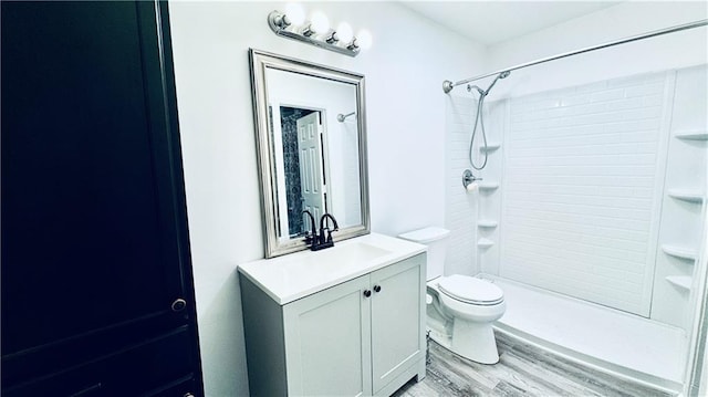 bathroom featuring vanity, a tile shower, toilet, and wood finished floors