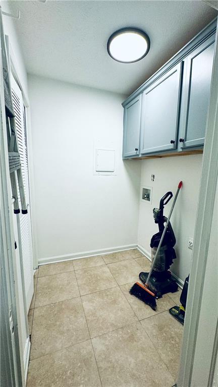 washroom with baseboards, a textured ceiling, light tile patterned flooring, hookup for a washing machine, and cabinet space
