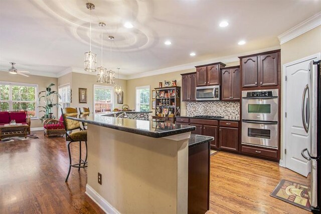 kitchen featuring hanging light fixtures, light hardwood / wood-style flooring, a kitchen bar, a center island with sink, and appliances with stainless steel finishes