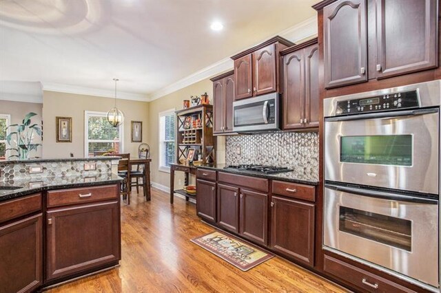 kitchen featuring dark stone countertops, light wood-type flooring, ornamental molding, appliances with stainless steel finishes, and decorative light fixtures