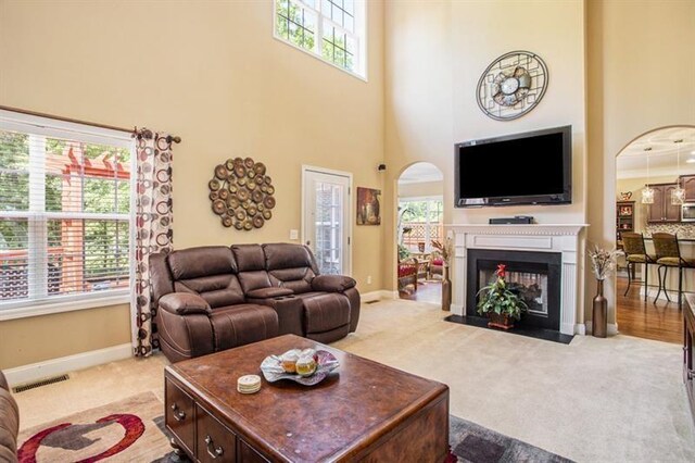 carpeted living room featuring a multi sided fireplace, a high ceiling, and plenty of natural light