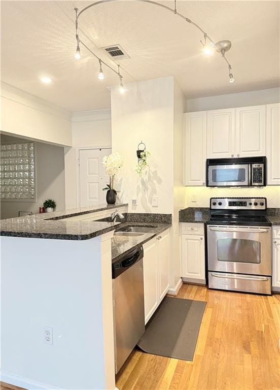 kitchen featuring kitchen peninsula, dark stone counters, stainless steel appliances, sink, and white cabinetry