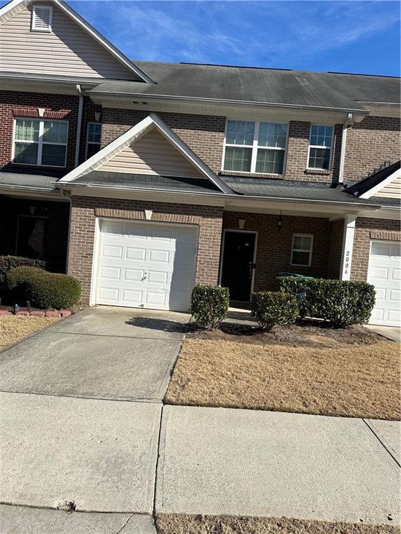 multi unit property featuring an attached garage, covered porch, concrete driveway, and brick siding