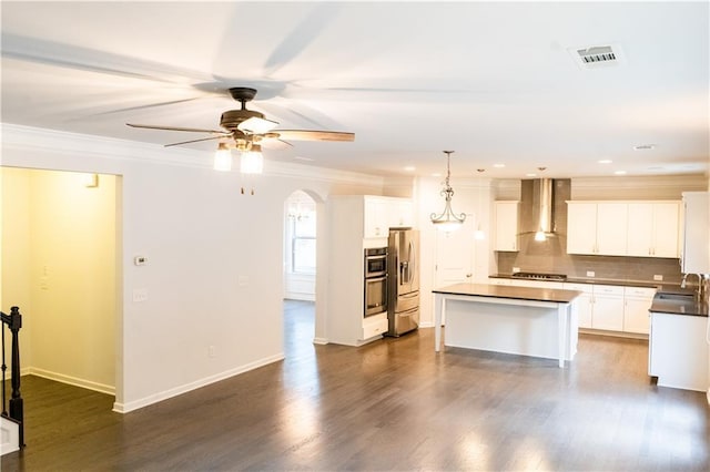 kitchen with a sink, wall chimney range hood, appliances with stainless steel finishes, a center island, and dark countertops