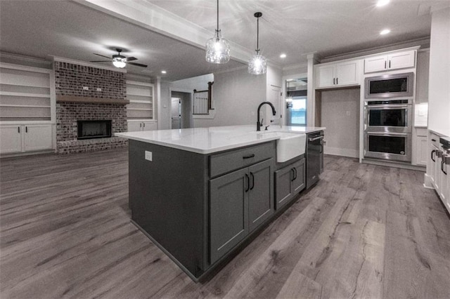 kitchen with white cabinets, built in features, stainless steel appliances, and a center island with sink