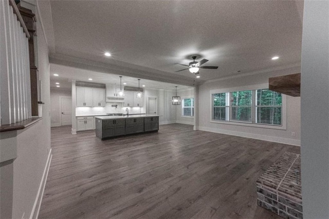 unfurnished living room with ceiling fan, sink, crown molding, and dark wood-type flooring