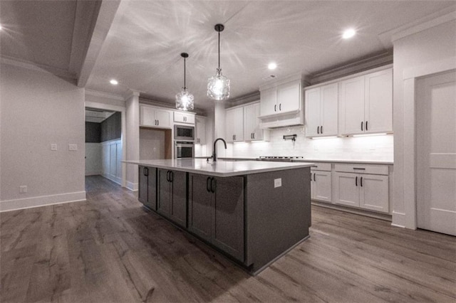 kitchen featuring sink, white cabinets, hanging light fixtures, and an island with sink