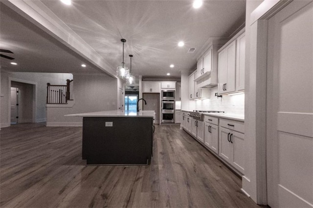 kitchen with stainless steel appliances, white cabinets, hanging light fixtures, and a kitchen island with sink