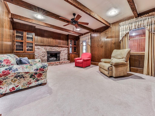 carpeted living room with a fireplace, beam ceiling, wooden walls, and ceiling fan