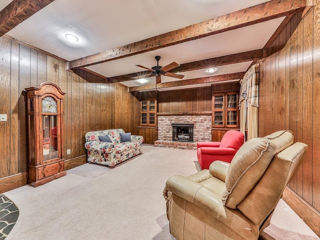 carpeted living room with beam ceiling, ceiling fan, a brick fireplace, and wooden walls