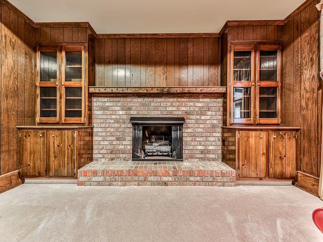 unfurnished living room featuring a brick fireplace, light colored carpet, and wood walls