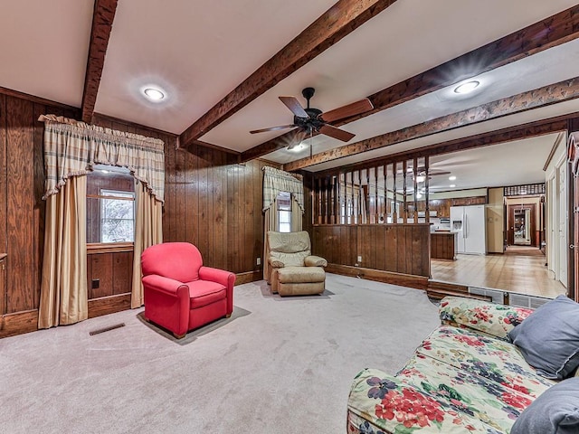 living room with beamed ceiling, carpet, ceiling fan, and wood walls