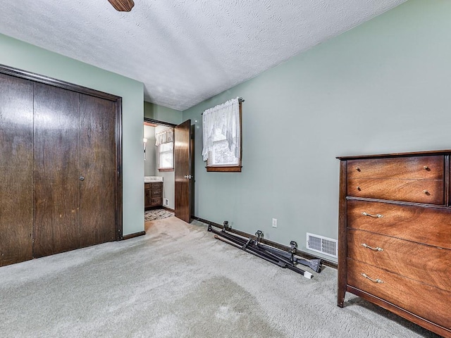 unfurnished bedroom featuring light colored carpet, ensuite bathroom, a closet, and a textured ceiling