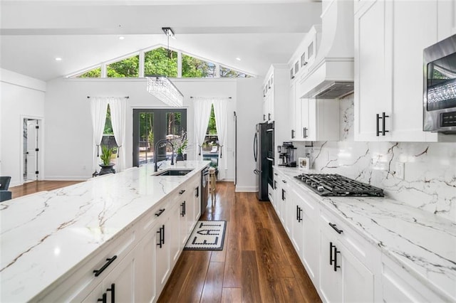 kitchen featuring light stone countertops, appliances with stainless steel finishes, a sink, custom range hood, and glass insert cabinets