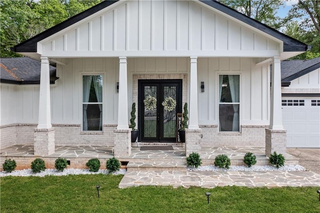 view of exterior entry featuring french doors, brick siding, a shingled roof, board and batten siding, and a porch