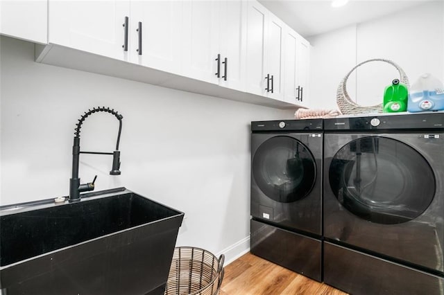 clothes washing area with washing machine and dryer, cabinet space, a sink, baseboards, and light wood finished floors
