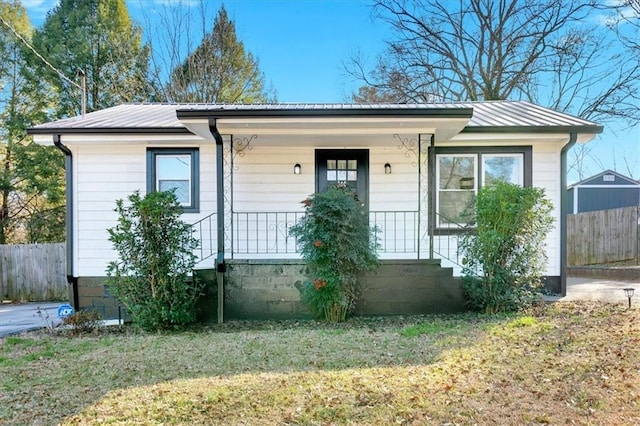 bungalow with covered porch, metal roof, a front lawn, and fence