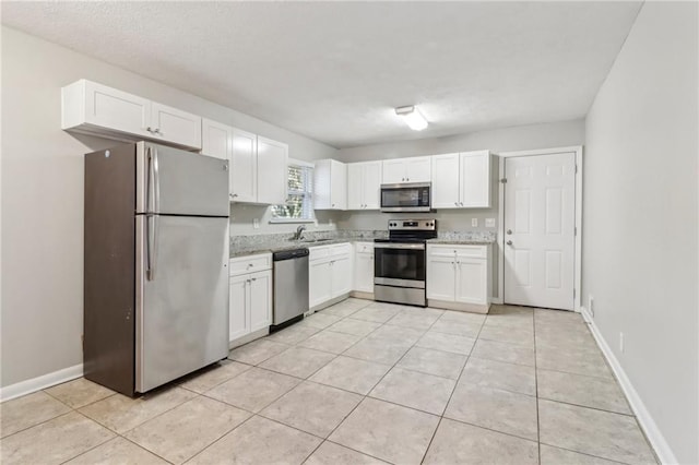 kitchen featuring sink, light stone counters, light tile patterned floors, appliances with stainless steel finishes, and white cabinets