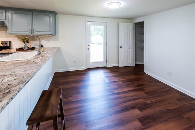 kitchen featuring light stone counters, dark hardwood / wood-style floors, decorative backsplash, gray cabinetry, and sink