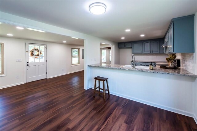 kitchen with kitchen peninsula, light stone countertops, tasteful backsplash, and dark hardwood / wood-style floors