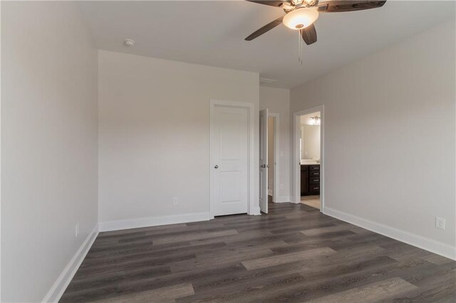 unfurnished bedroom featuring dark wood finished floors, baseboards, ensuite bath, and ceiling fan