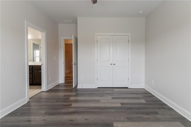 unfurnished bedroom with a closet, wood finished floors, ensuite bathroom, and baseboards