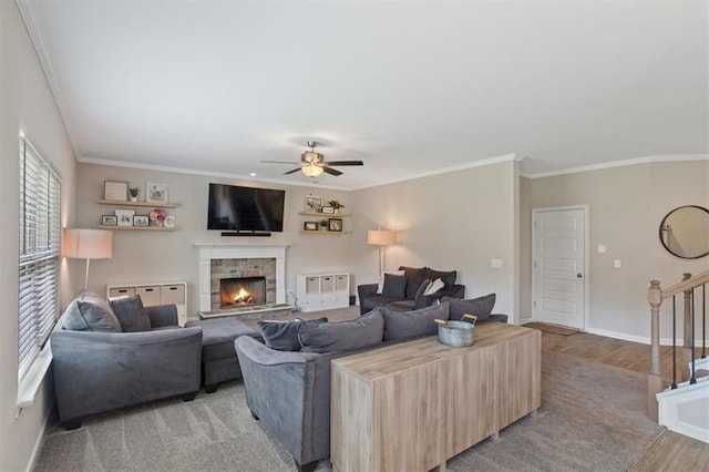 living area with light wood finished floors, crown molding, a ceiling fan, stairs, and a fireplace