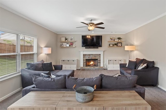 living area featuring ceiling fan, carpet, baseboards, a stone fireplace, and ornamental molding