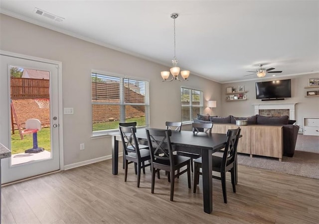 dining area with wood finished floors, crown molding, a chandelier, a ceiling fan, and a fireplace
