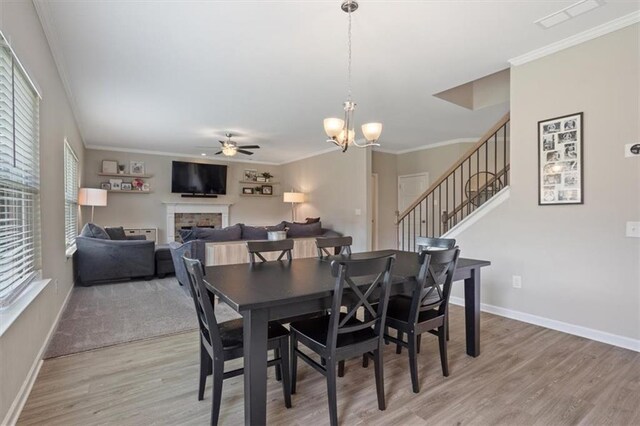 dining room featuring ceiling fan, light wood-style floors, a fireplace, stairs, and ornamental molding