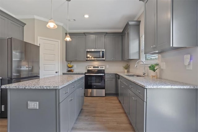 kitchen featuring appliances with stainless steel finishes, gray cabinets, a sink, ornamental molding, and a center island