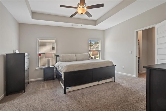 carpeted bedroom with baseboards, a tray ceiling, and a ceiling fan