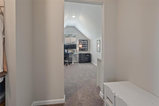 hall featuring light colored carpet, lofted ceiling, an office area, and baseboards