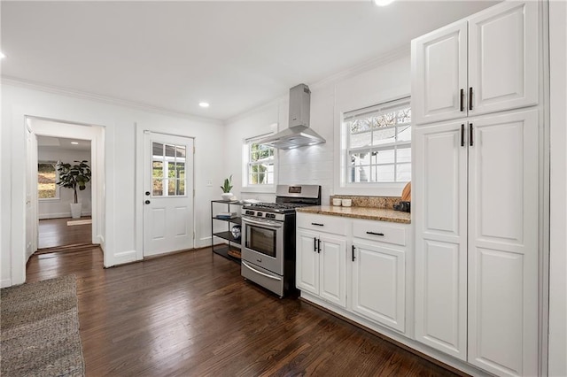 kitchen featuring dark wood finished floors, stainless steel range with gas stovetop, ornamental molding, white cabinets, and wall chimney range hood