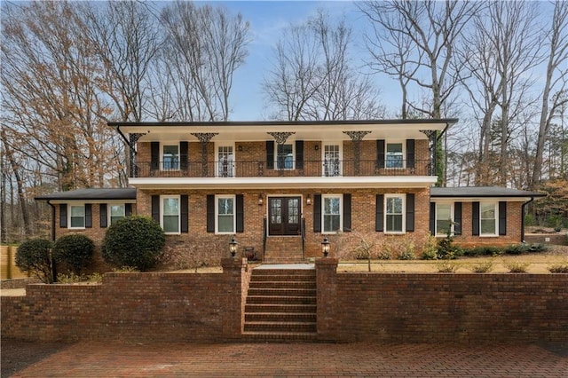 view of front facade featuring french doors, brick siding, and a balcony