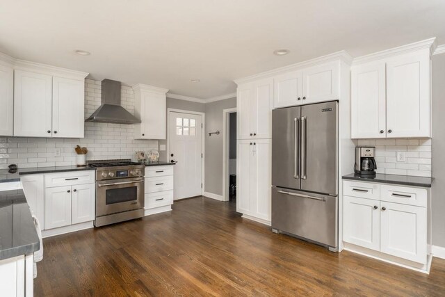 kitchen with premium appliances, dark countertops, dark wood-style flooring, and wall chimney exhaust hood