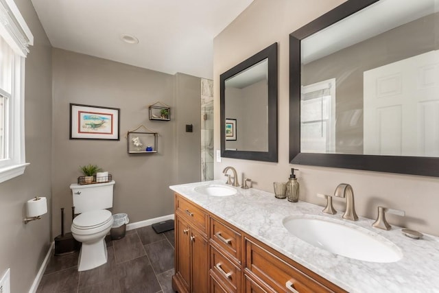 bathroom with double vanity, a sink, toilet, and baseboards