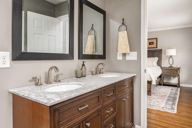 ensuite bathroom with wood finished floors, double vanity, ornamental molding, and a sink