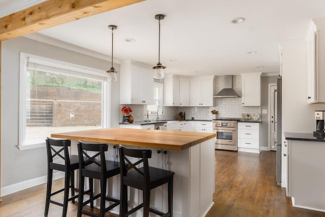 kitchen with high end range, wall chimney exhaust hood, white cabinets, and backsplash