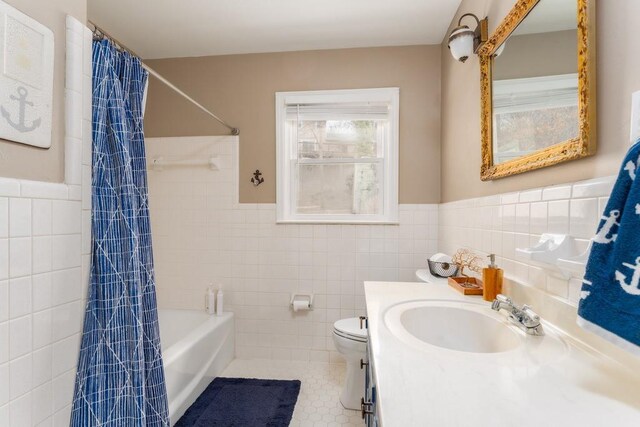 full bath with toilet, a wainscoted wall, tile walls, tile patterned floors, and shower / bath combo with shower curtain