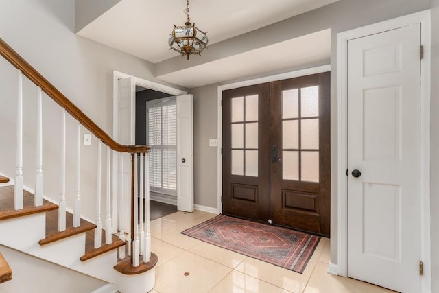 entrance foyer featuring french doors, a notable chandelier, light tile patterned floors, stairway, and baseboards