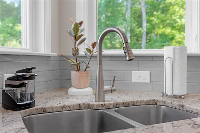 room details featuring a sink, light stone countertops, and tasteful backsplash