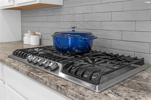 room details with light stone counters, decorative backsplash, white cabinetry, and stainless steel gas stovetop
