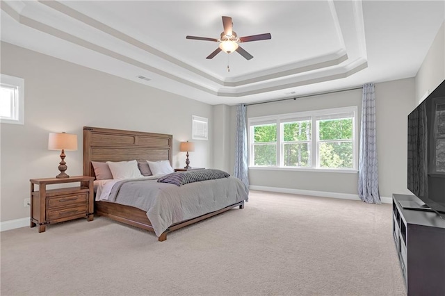 bedroom featuring a fireplace, light carpet, baseboards, a raised ceiling, and a ceiling fan