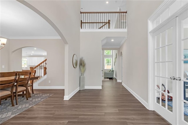 foyer with a towering ceiling, arched walkways, wood finished floors, baseboards, and ornamental molding