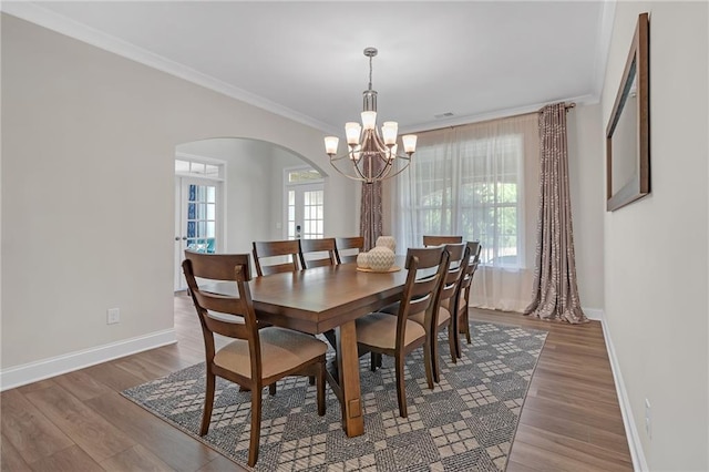 dining space with arched walkways, wood finished floors, baseboards, an inviting chandelier, and ornamental molding