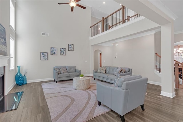 living room featuring visible vents, wood finished floors, a high ceiling, arched walkways, and ceiling fan with notable chandelier