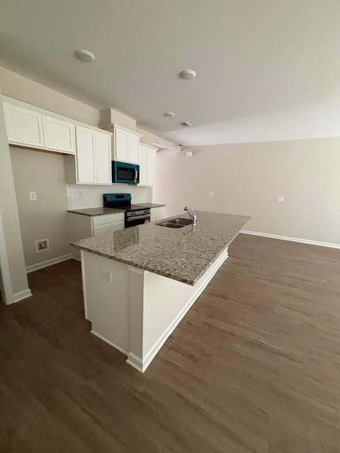 kitchen featuring dark stone counters, black appliances, white cabinets, a center island with sink, and sink