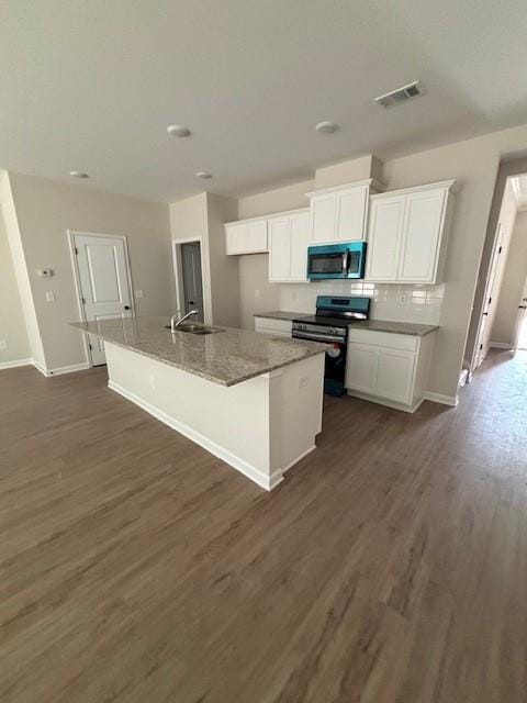 kitchen with black stove, white cabinetry, a kitchen island with sink, and dark stone counters